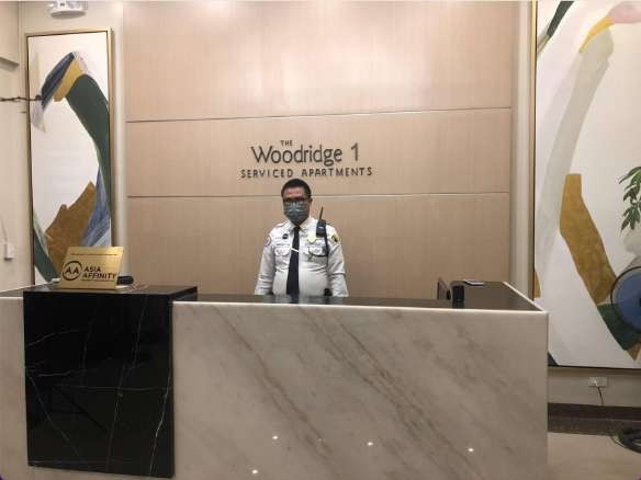 馬尼拉 Enderun 學生宿舍 Woodridge 的大理石櫃台,牆上寫著 Woodridge 1 Serviced Apartments,櫃台後站著一位保全