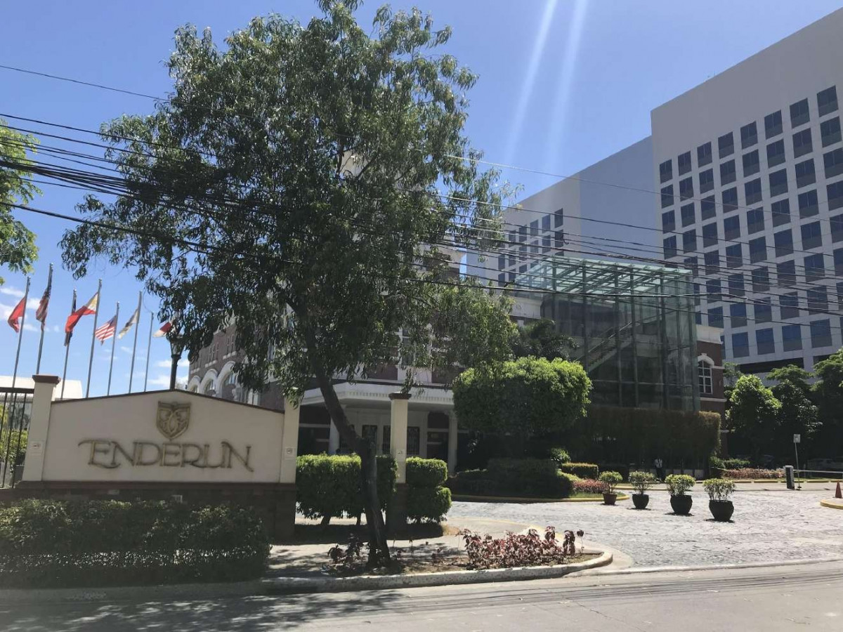 馬尼拉 Enderun 校園入口,矮牆上有 ENDERUN 校名招牌,旁邊是旗桿和大樹,後方是玻璃帷幕高樓