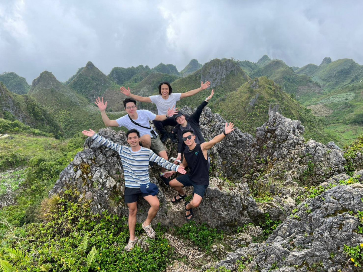 四位學生在 Osmeña Peak 山頂的灰色岩石上張開雙手，背後是一座座尖尖的綠色山丘和雲層