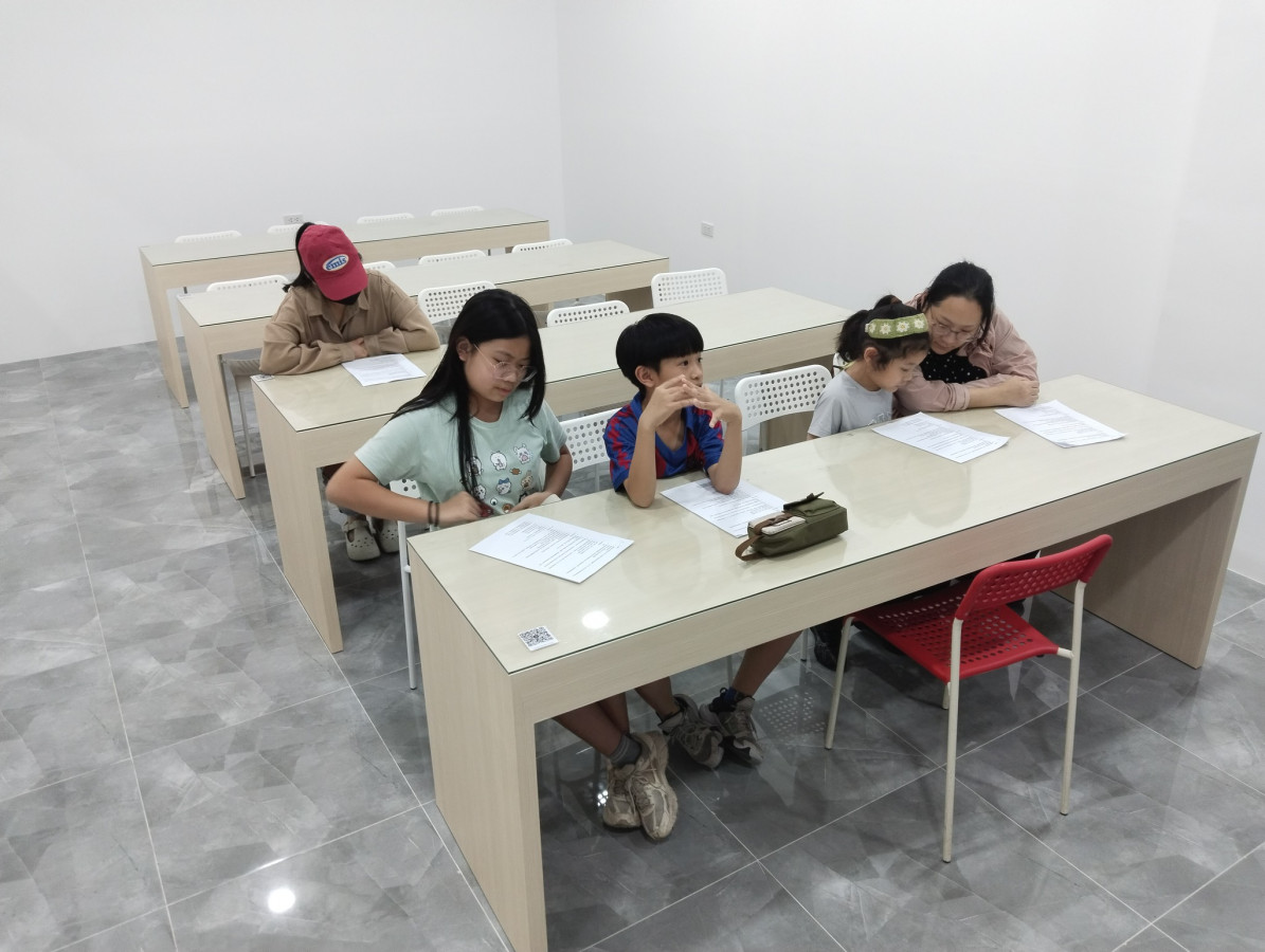 克拉克 TALK 語言學校新校區的新生說明會，一位大人和三個孩子並排坐在長桌前看說明文件