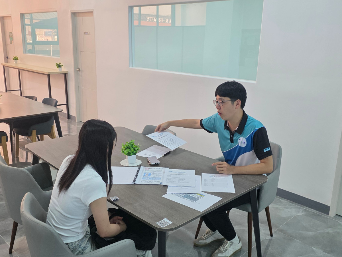 克拉克 TALK 語言學校新校區，穿學校制服的職員坐在長桌對面，拿著一張張文件向新生說明