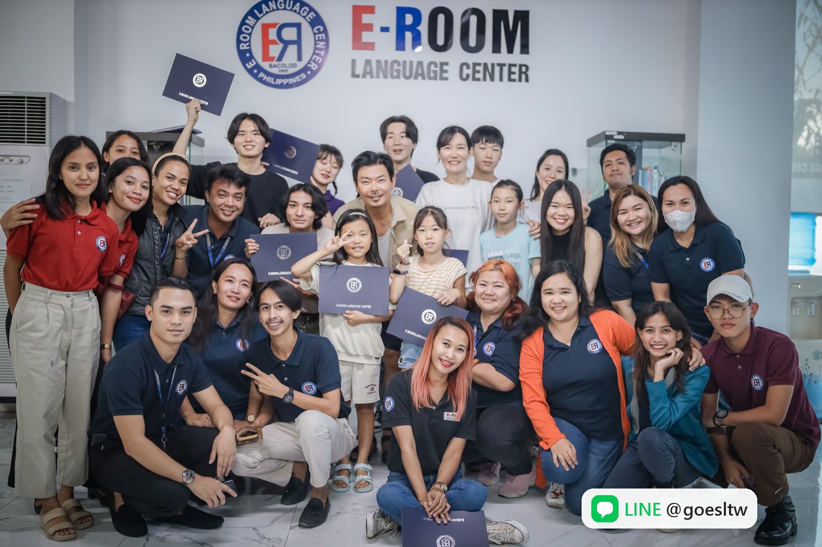 EROOM 學生與職員拿著證書在 E-ROOM 校名牆前合照
