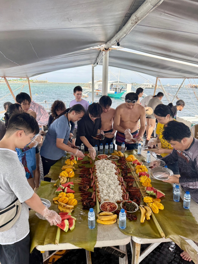 宿霧 CPILS 語言學校的學生跳島,在船上圍著鋪滿香蕉葉的長桌,桌上擺著烤肉串、米飯和水果