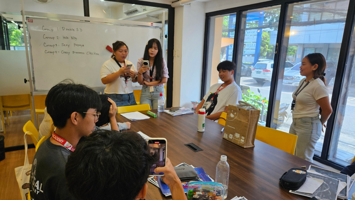 宿霧 ICL 語言學校落地窗教室裡的團體課，白板寫著分組名單，學生圍著長桌分組討論