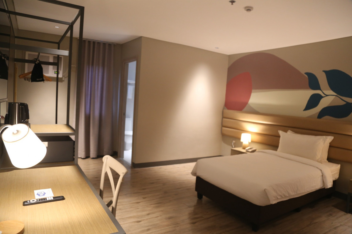宿霧 CBOA 校外飯店宿舍 Ocean Suites 的高級單人房，一張大床、書桌和檯燈，牆邊有開放式吊衣架，沒有人