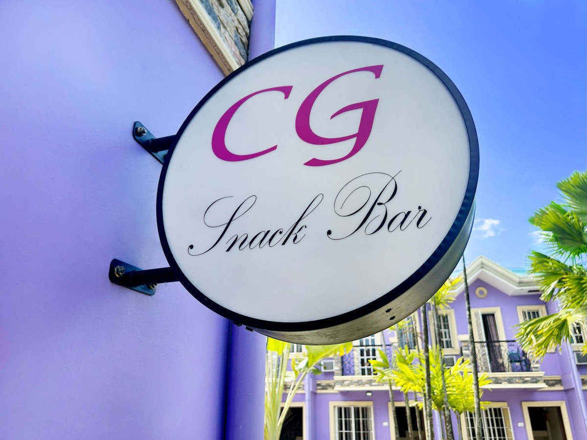 宿霧 CG SPARTA 校區紫色牆上的 CG Snack Bar 圓形招牌,後方是紫色連排建築和棕櫚樹