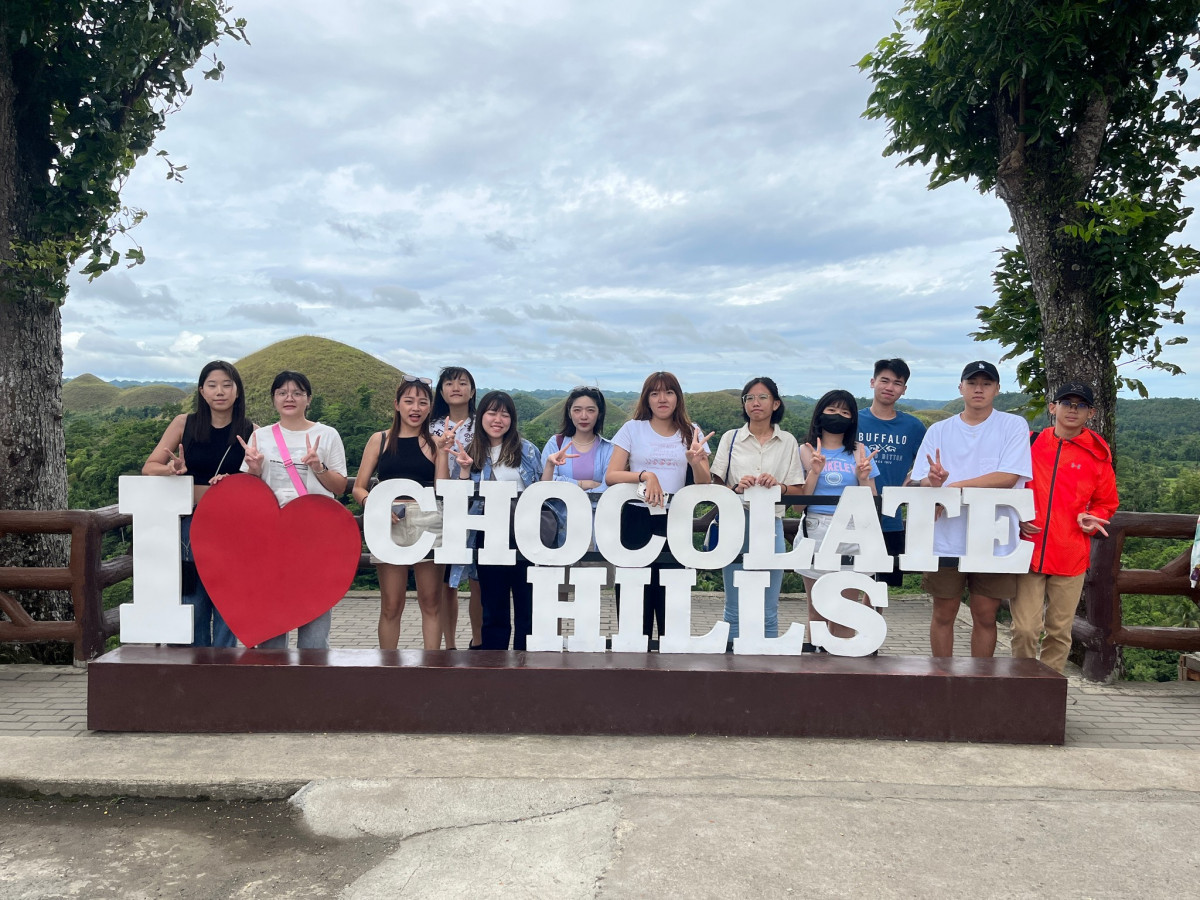 宿霧 GLC 語言學校的戶外教學，十幾位學生站在薄荷島 I love Chocolate Hills 字牌後合照，背景是一座座巧克力山