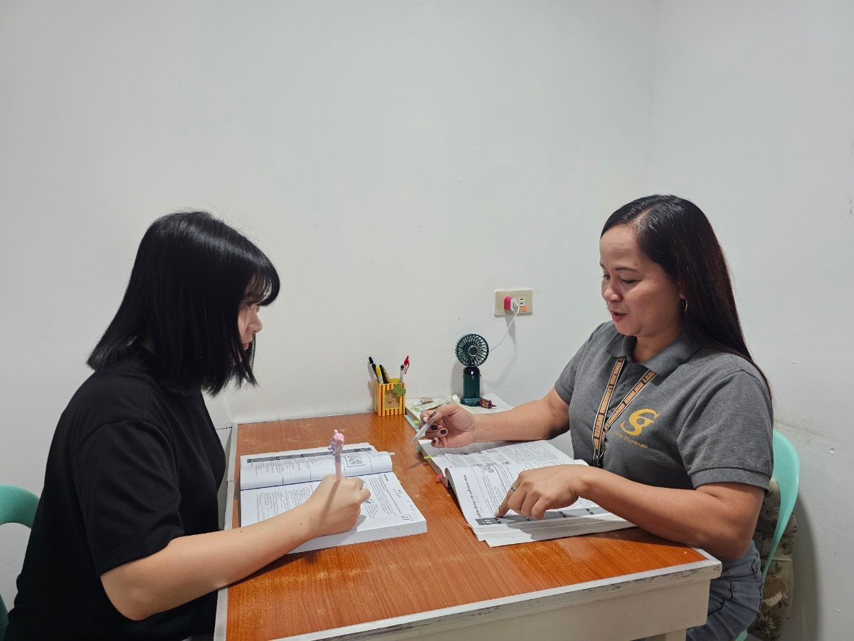 克拉克 GS 語言學校的一對一小教室,穿灰色 POLO 衫、掛識別證的女老師指著課本講解,學生低頭邊聽邊寫