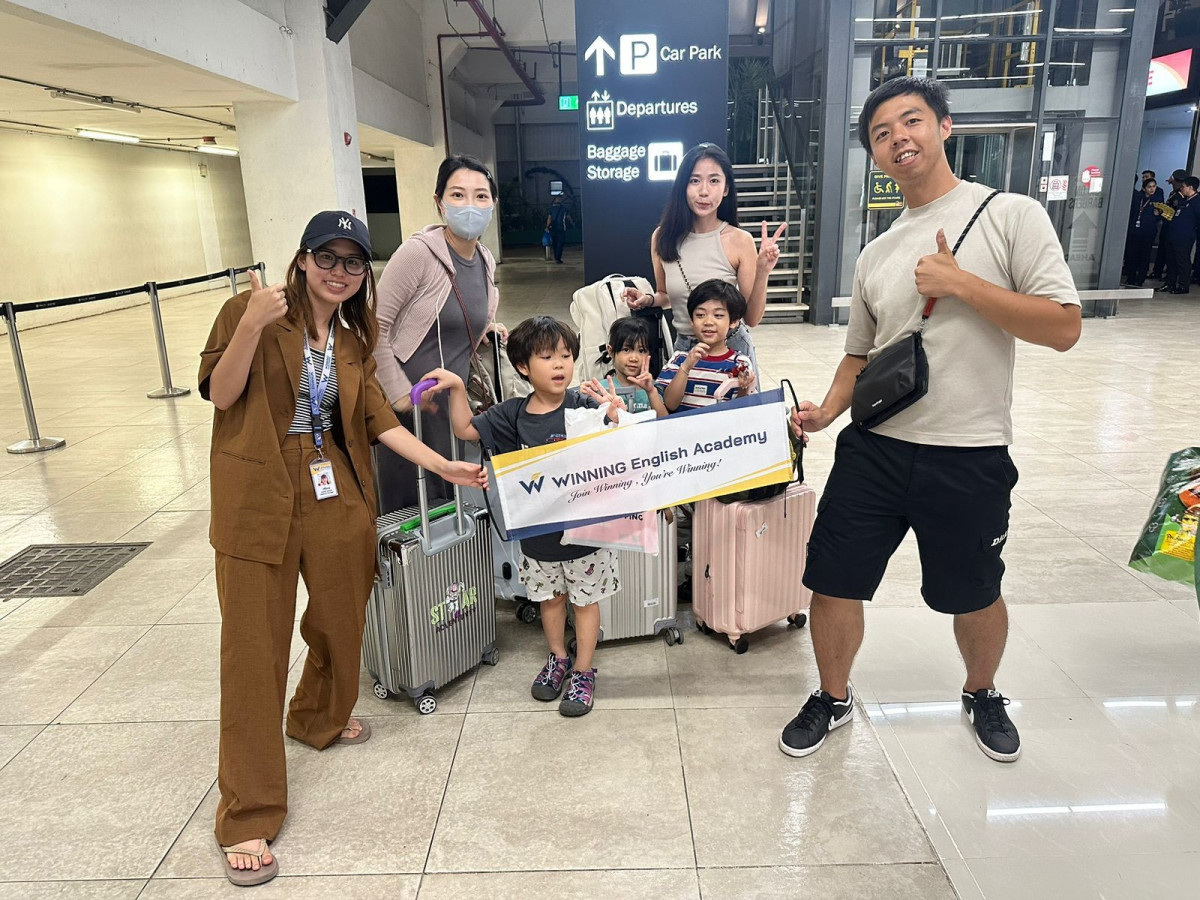 宿霧 WINNING 語言學校接機人員在機場拉著 WINNING English Academy 布條,跟帶著小孩和行李箱的大人合照
