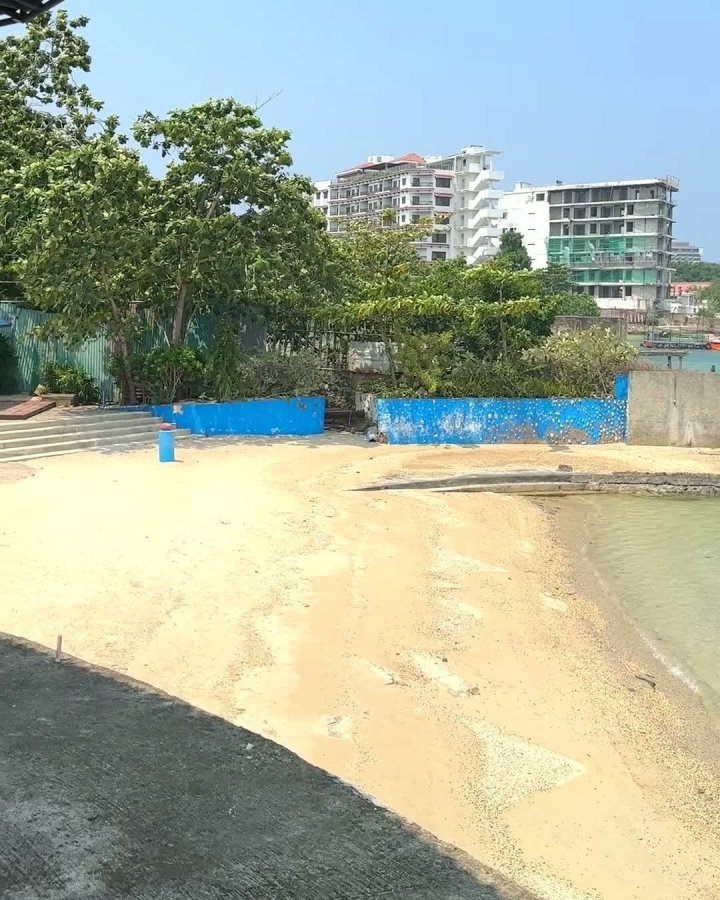 宿霧 CBOA 校內宿舍所在的渡假村海邊,一小片沙灘延伸到淺水,岸邊有藍色矮牆和樹叢,後方是幾棟白色高樓