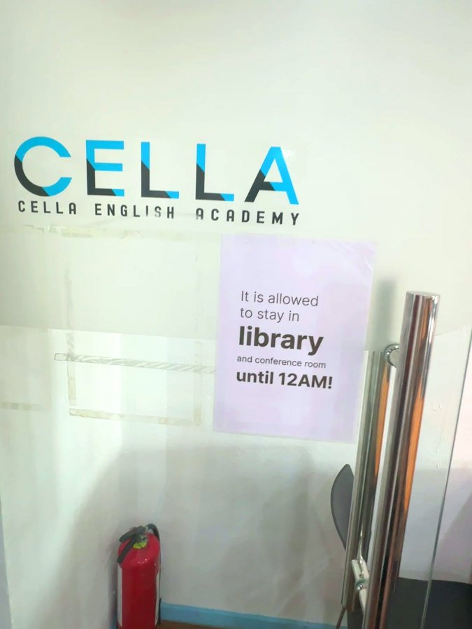 宿霧 CELLA PREMIUM 校區圖書館玻璃門旁,牆上有 CELLA 標誌和紫色公告,寫著圖書館和會議室可以待到 12AM