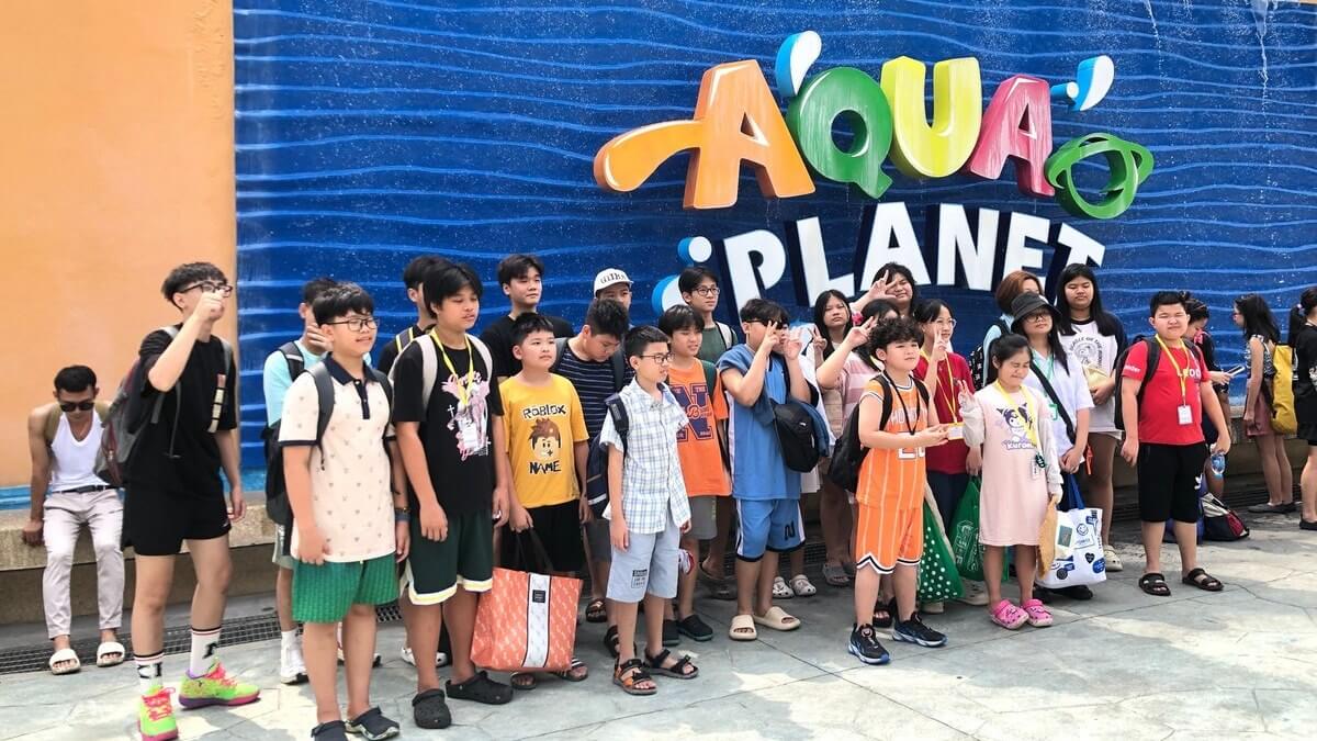 HELP 克拉克營隊學生在 Aqua Planet 水上樂園招牌前合照（往年營隊，2024 年）