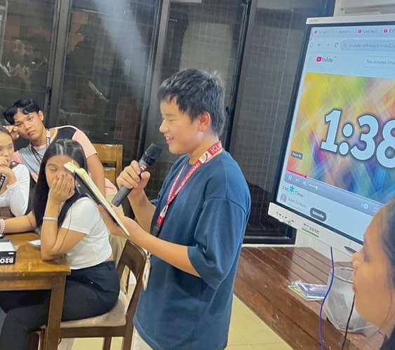 學生拿麥克風上台發表,旁邊螢幕在計時(往年營隊)